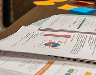 a stack of paper, reports, and sticky notes are spread out across a table.